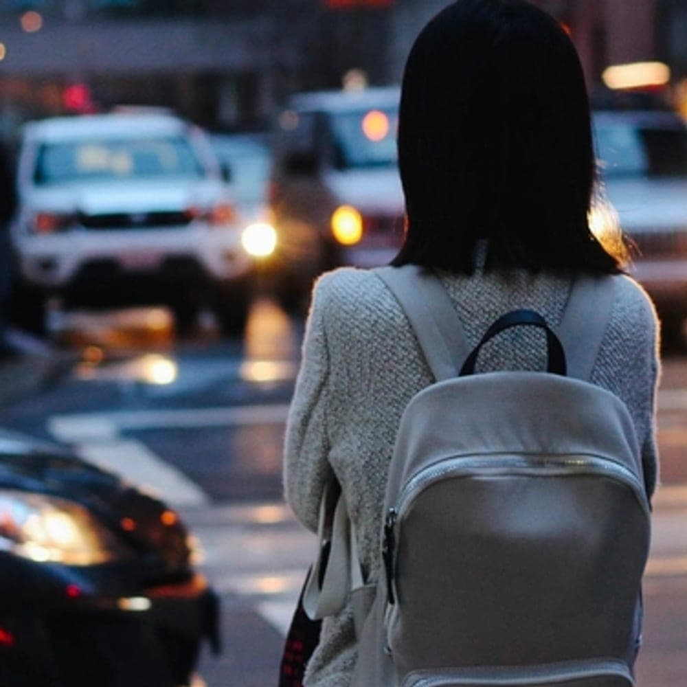 Persona cruzando la calle con una mochila clara al hombro